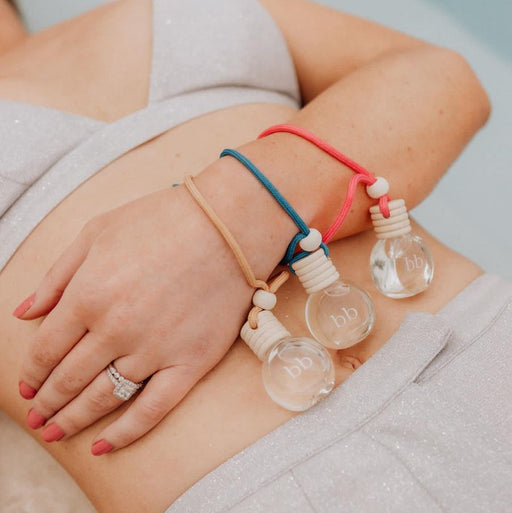 Close-up of a person's arm with three bracelets featuring clear bottle-shaped charms.