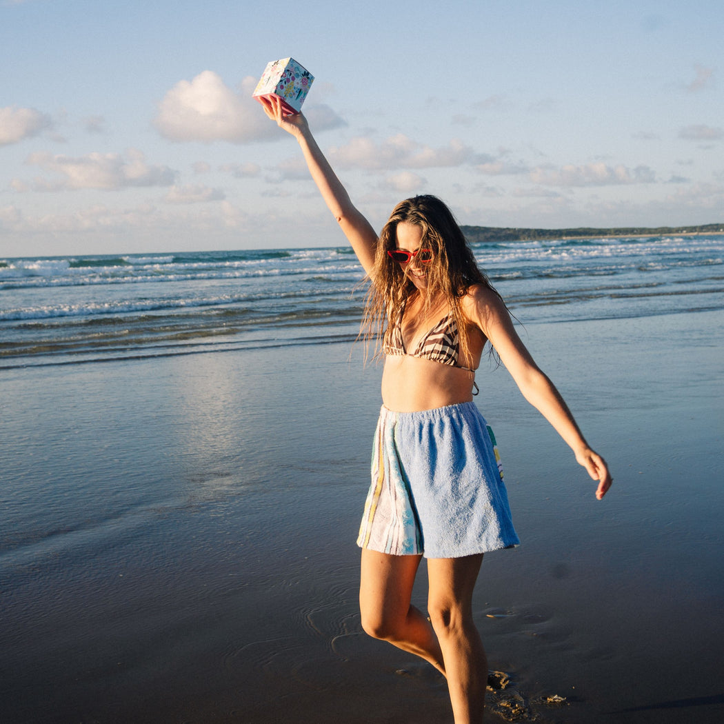 Woman on a beach holding a box, with ocean waves and sky in the background