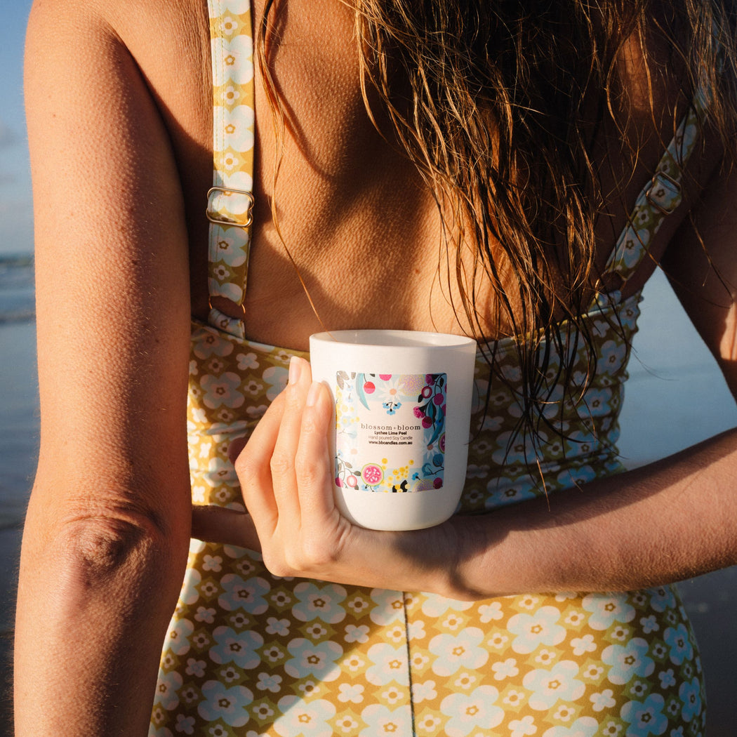 Person holding a white candle with a colorful label on a beach
