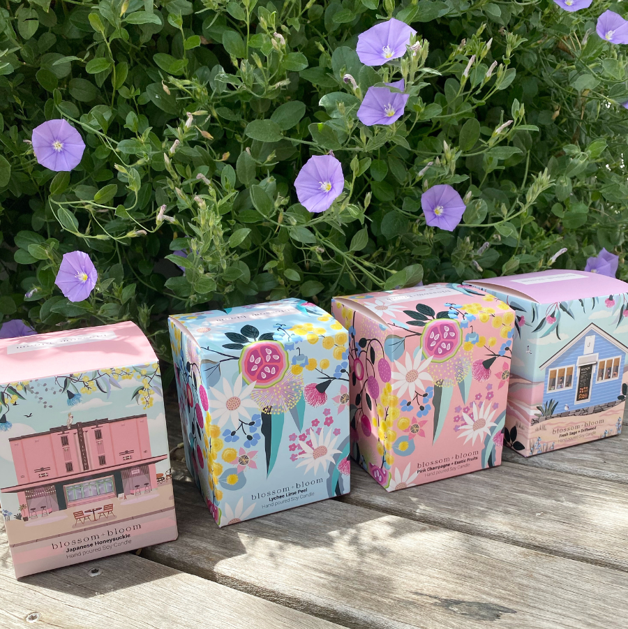 A set of four candles with floral patterns, displayed on a wooden surface with a background of purple flowers.
